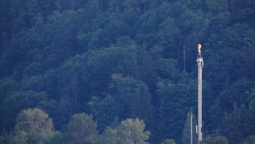 Birds fly past a tall pipe that has a flame coming out of it in the mountains