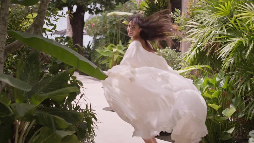 Smiling woman running in light dress amid tropical vegetation
