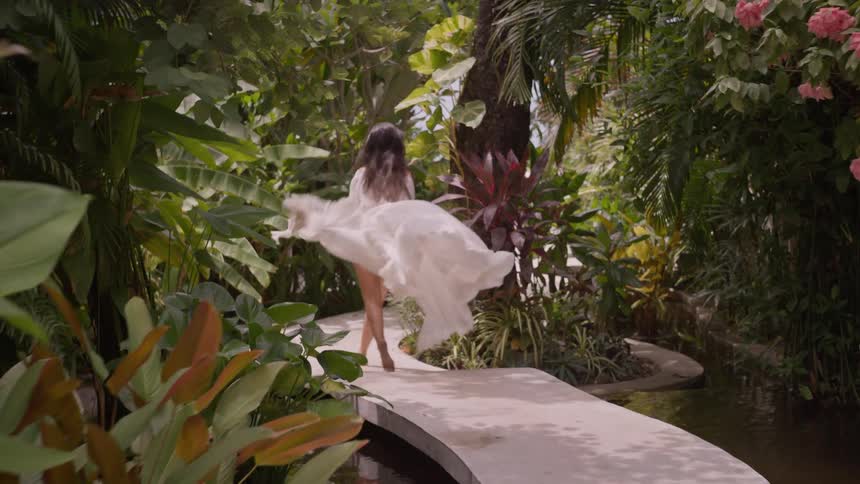 A woman in a white dress runs down a path in a garden