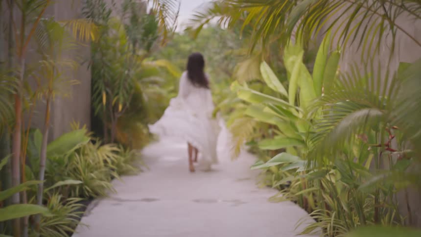 A young lady running on a path with plants lining both sides of the wall during a vacation at midday