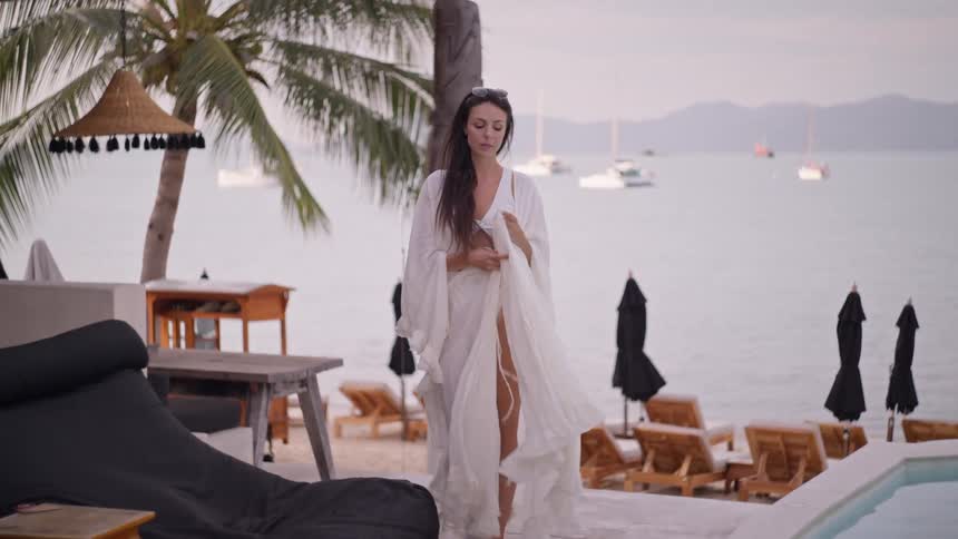 A young woman dressed in white walking along the waterfront at a resort by the poolside at midday enjoying her time