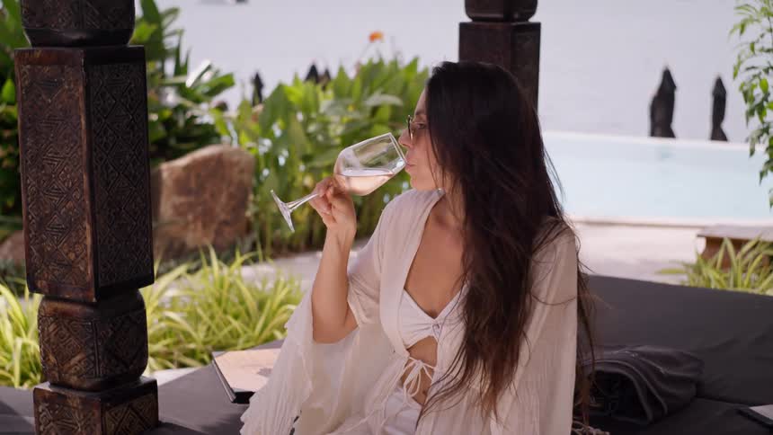 Woman in sunglasses enjoys a glass of ros wine by the pool