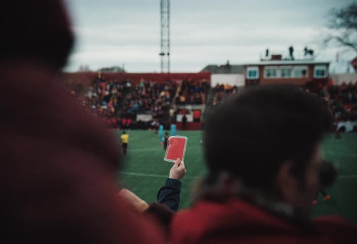 Fan holds up a red card in the stands of a crowded soccer stadium while the game goes on in the field