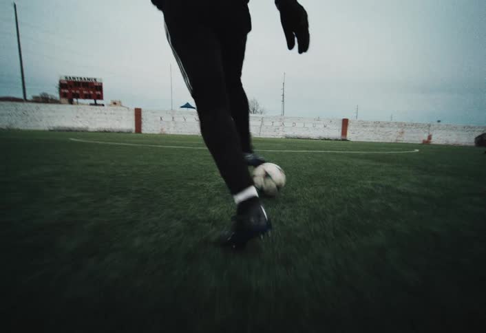 A person in athletic gear stands on a grassy field controlling a ball with their feet