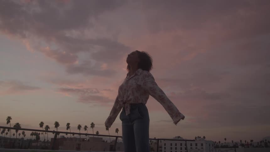 The woman stands on the rooftop with her arms stretched out
