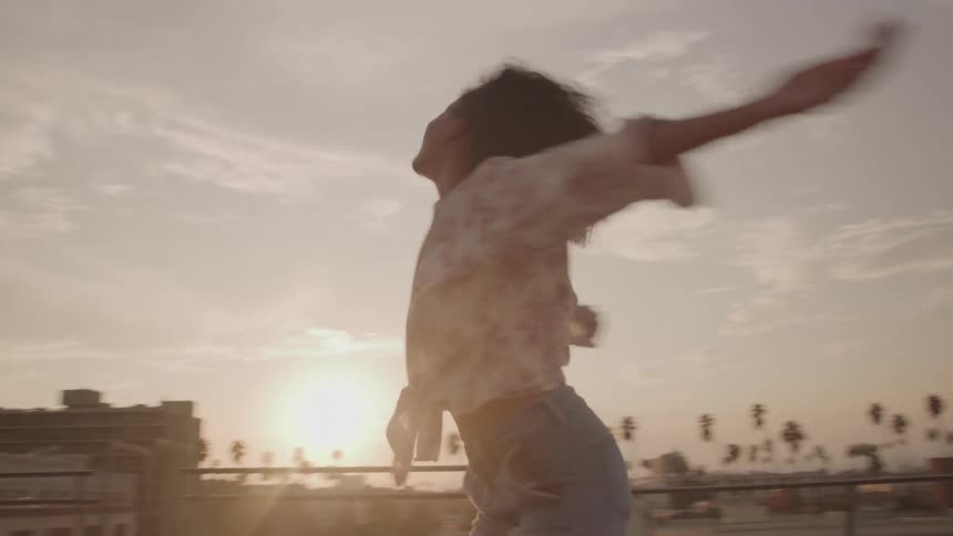 A joyful woman on a rooftop with arms wide open at sunset