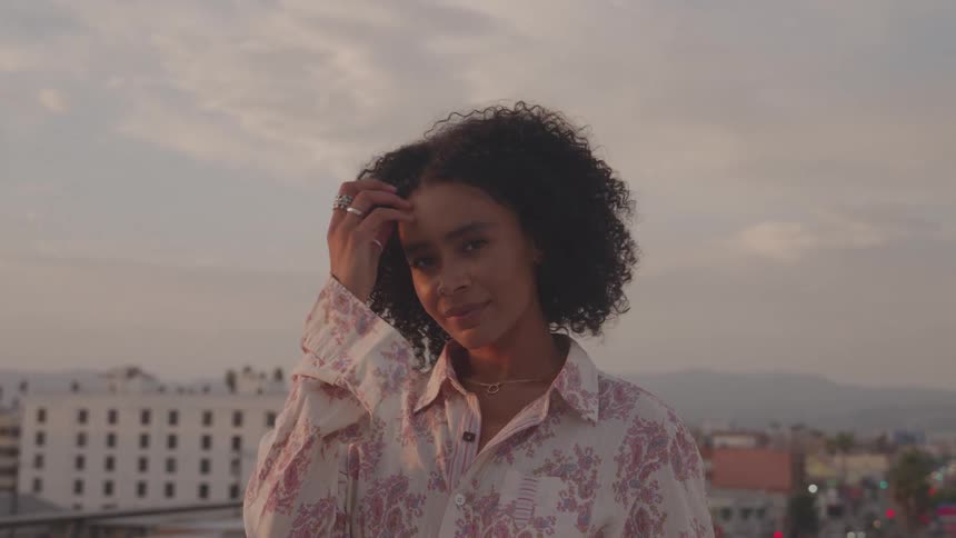 Woman with curly hair posing outdoors with the city in the background