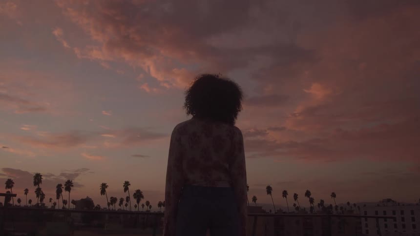 Close up of a young black woman watching the skies while standing on a rooftop at sunset