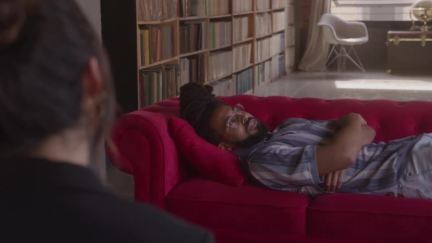 Man laying on red couch talking to his therapist during a session