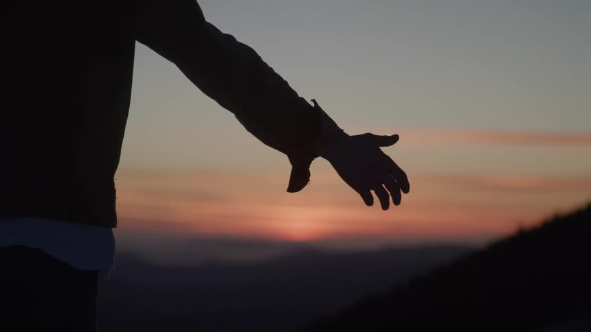 Close up of a young man spreading his arms while standing outdoors at sunset