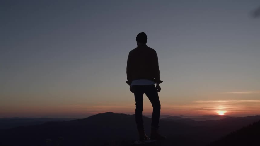 A man watches the sinking sun his silhouette quiet and pensive as dusk settles