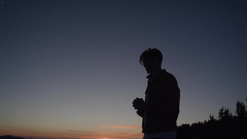 A persons body is shown in a silhouette against the sky in the sunset on a natural landscape setting