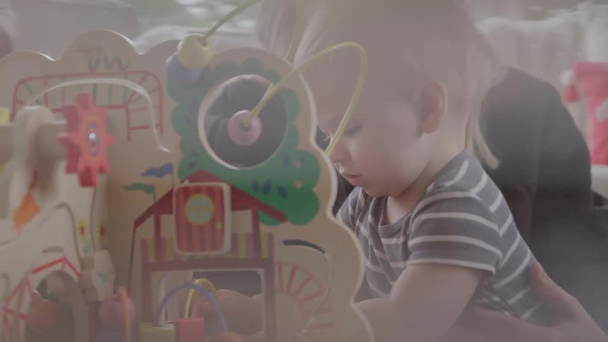 Woman lovingly watching a baby playing with an educational toy
