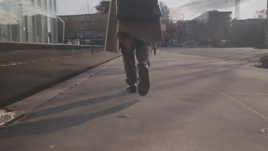 Close up of a mans legs as he walks on a sidewalk in a metropolitan city during daytime
