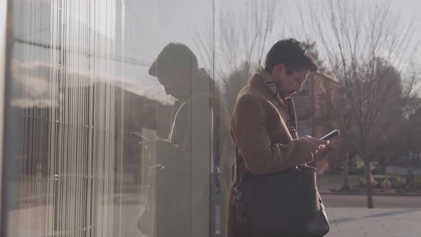 The man texts on his phone by the building