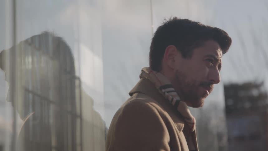 Man in a beige coat leaning against glass reflecting his silhouette