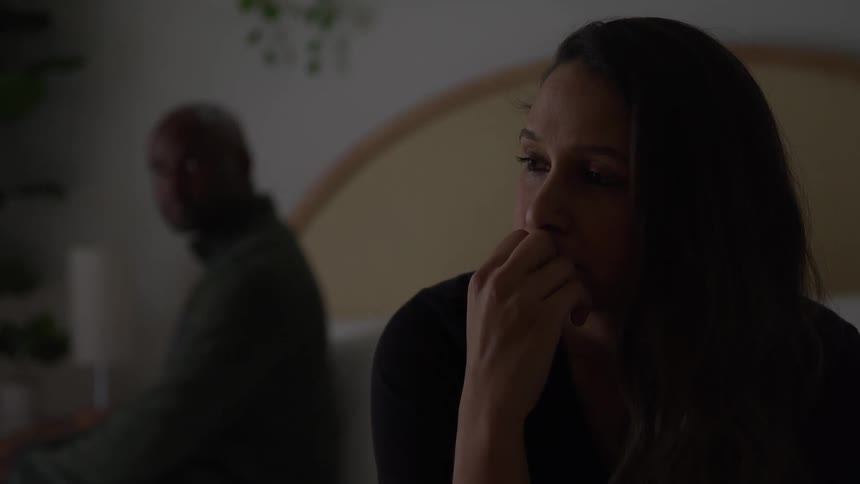 Woman with a worried expression looks to the side while a man is blurred in the background