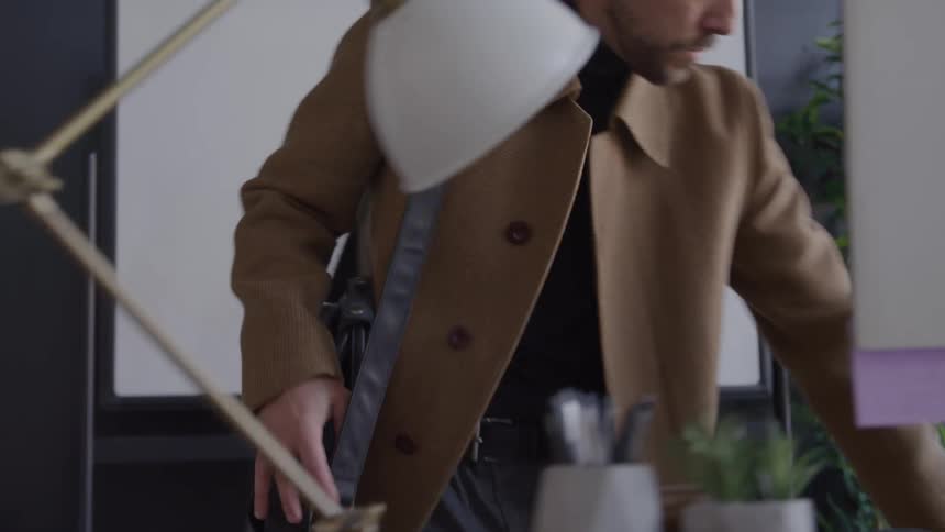 A person walks into a room sets down an item on a desk and sits down in a chair at the desk with a laptop pc