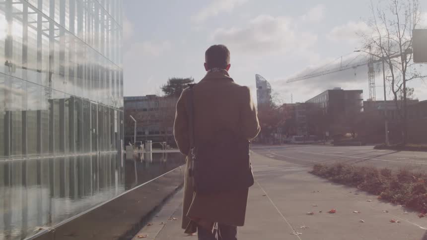 Person walking on a sunny urban street with a shoulder bag
