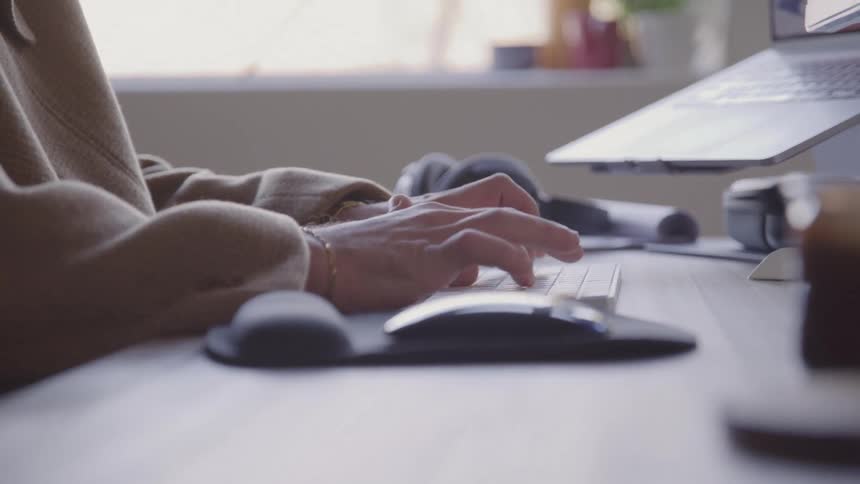 Close up of a young man typing while using an external keyboard for a computer on a desk indoors during daytime
