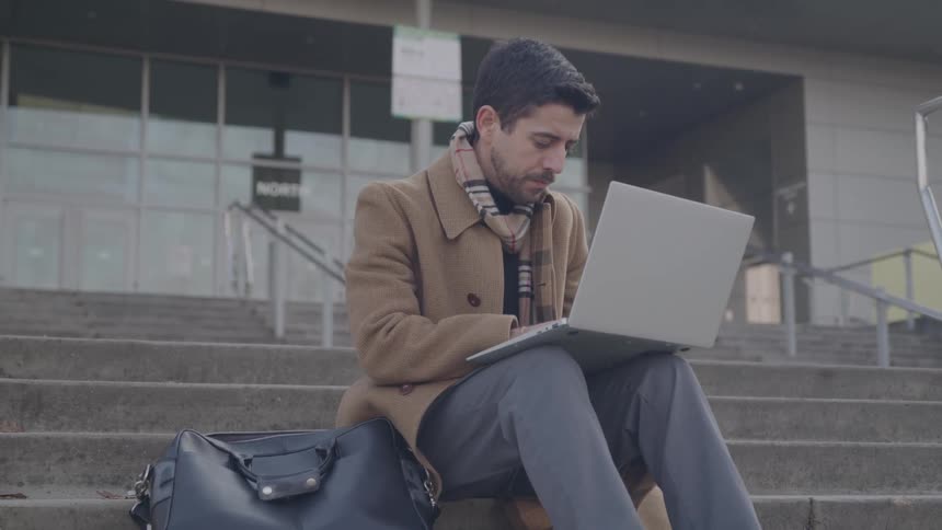 The man is using his laptop outside the building entrance