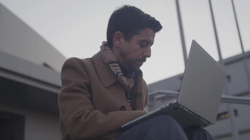 The man is typing on his laptop outside