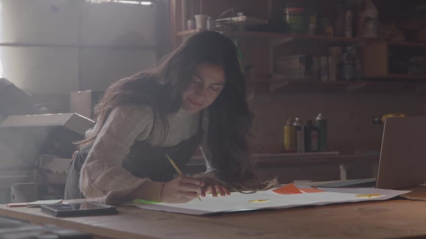 A young woman leans over a table and write something on a paper sheet