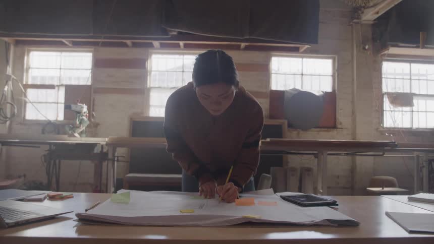 The woman is writing on blueprints in the workshop
