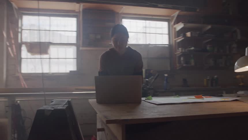 A young asian woman working with a laptop computer at a workdesk in a workshop during daytime