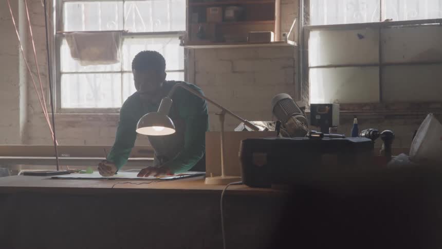 A young black man working at a table in a workshop during daytime