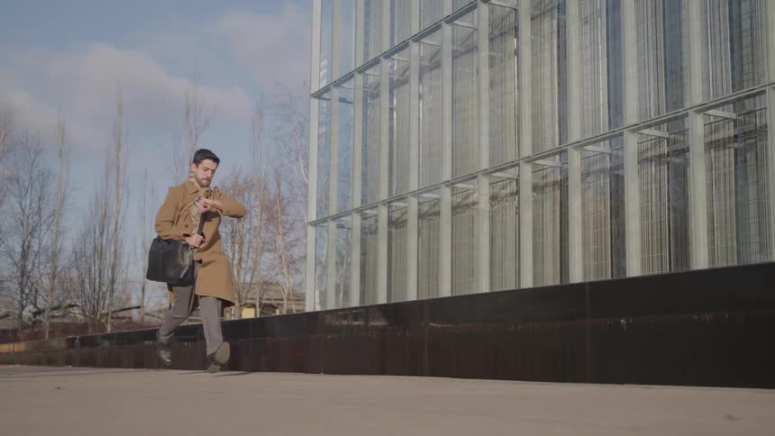 Man looking at his watch and running while holding a leather bag