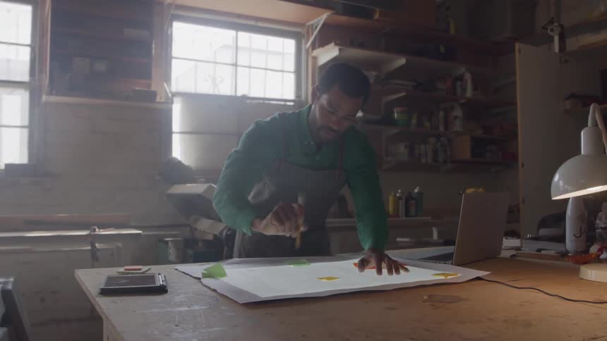 The man uses a pencil to write on the blueprints