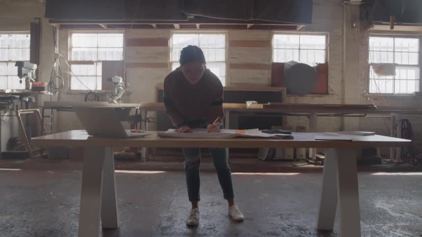 Woman standing and working at a large wooden table in a workshop