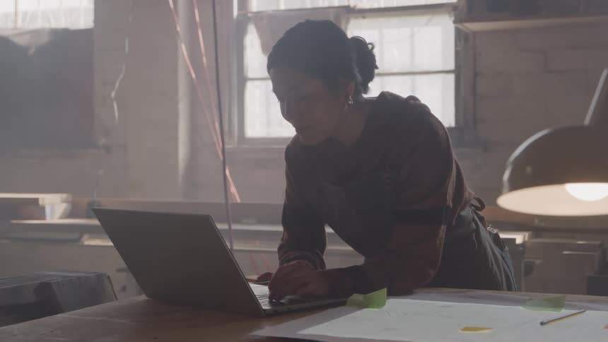 Woman leaning over the table typing on a laptop