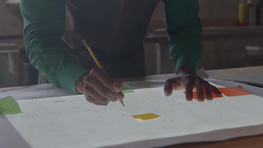 Closeup of male hands sketching on a large sheet of paper with a pencil overlaid with colorful sticky notes
