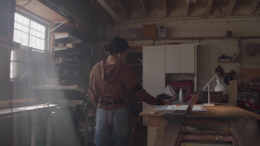 Woman walking towards a laptop and a blueprint on a table