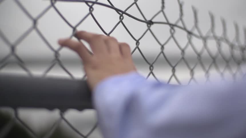 A hand gripping a chain link fence