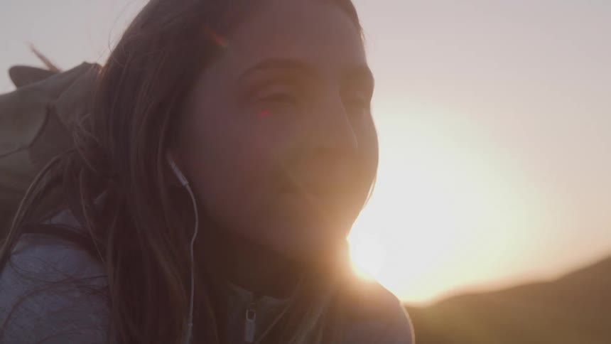 Woman with earphones gazes at the sunset outdoors