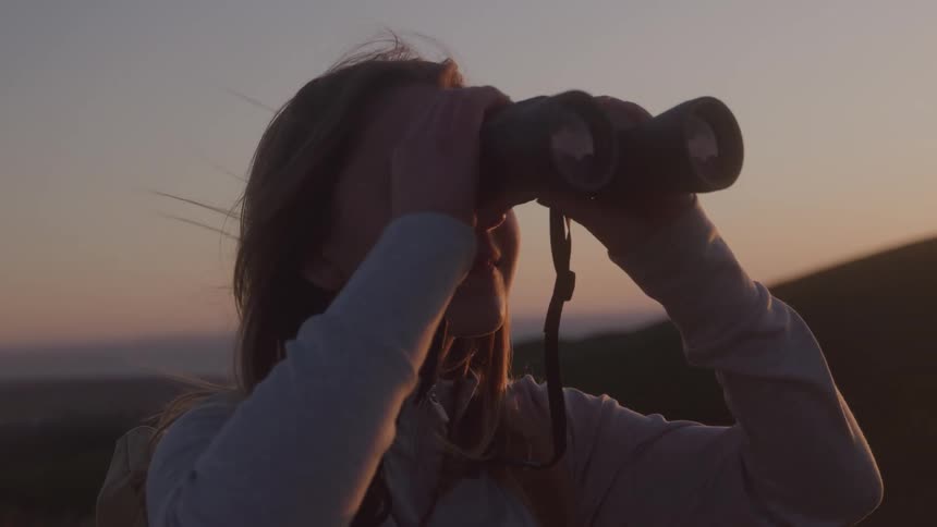 Woman observes the horizon with binoculars at sunset