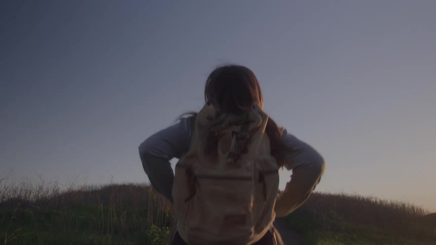 Young woman hiking through mountainous terrain at midday carrying a backpack under clear skies
