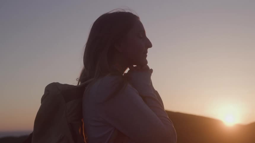 Sunset lights the silhouette of a woman with a backpack