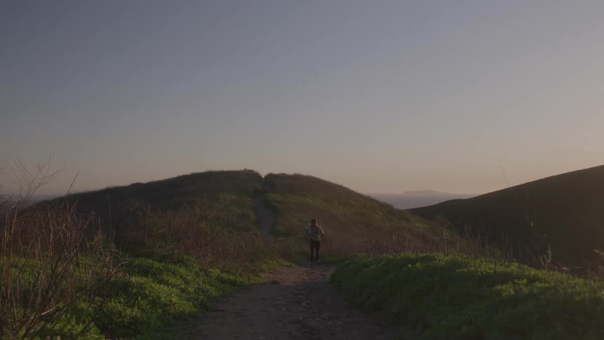A woman walks along a path on a hillside toward the camera