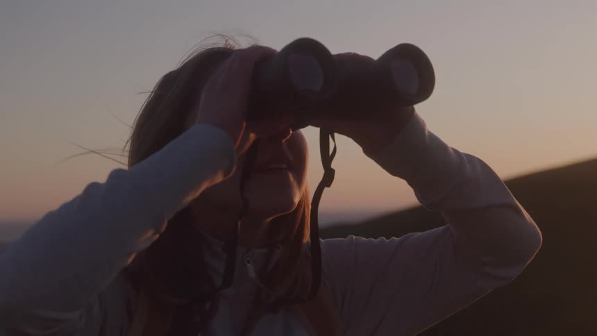 Woman looks at the horizon with binoculars at sunset