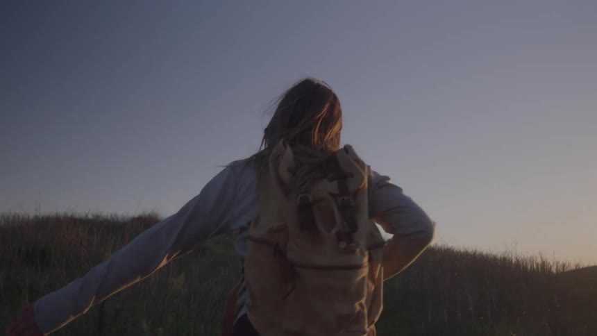 A young woman walking at a grass land with a backpack and a long sleeve shirt