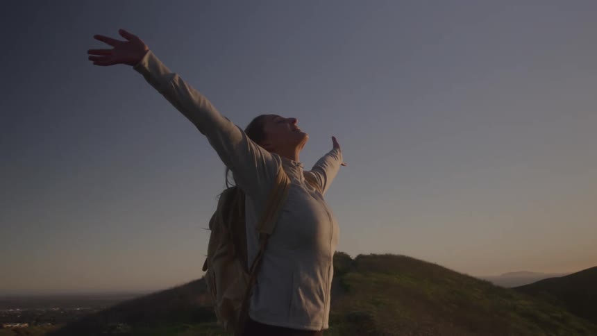 Woman on a mountain in the late afternoon opening her arms