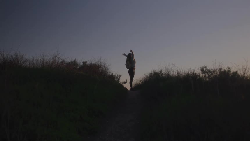 Woman opens her arms on a trail at dusk silhouetted against the sky