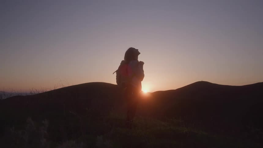 Silhouette of a woman with a backpack watching the sunset over the mountains