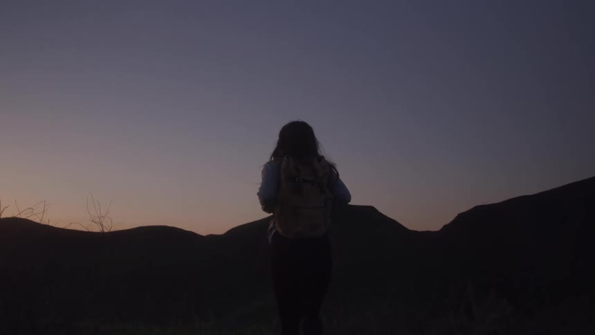 A woman hiking with a backpack in a mountainous landscape at dusk
