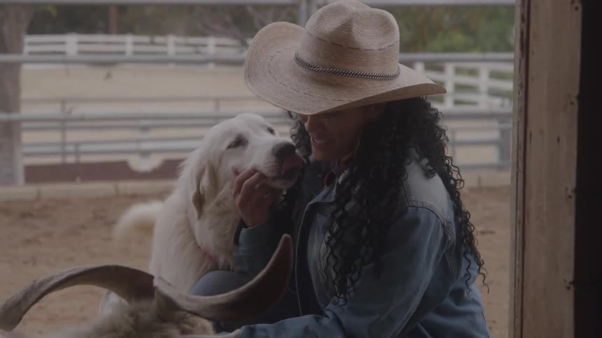 Person wearing a straw hat petting a white dog in a corral