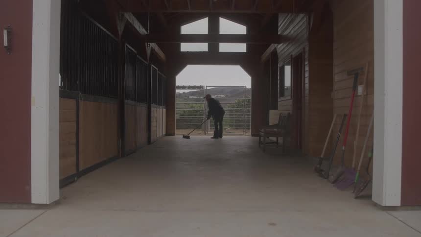 Person sweeping interior long corridor of a barn